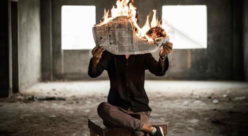 man sites in chair while burning a newspaper