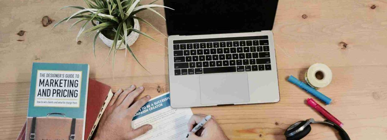 hand holding notepad next to computer and marketing book