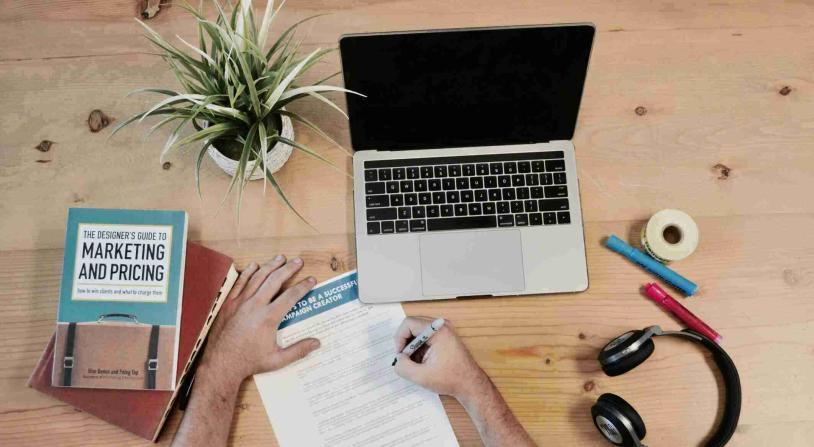 hand holding notepad next to computer and marketing book